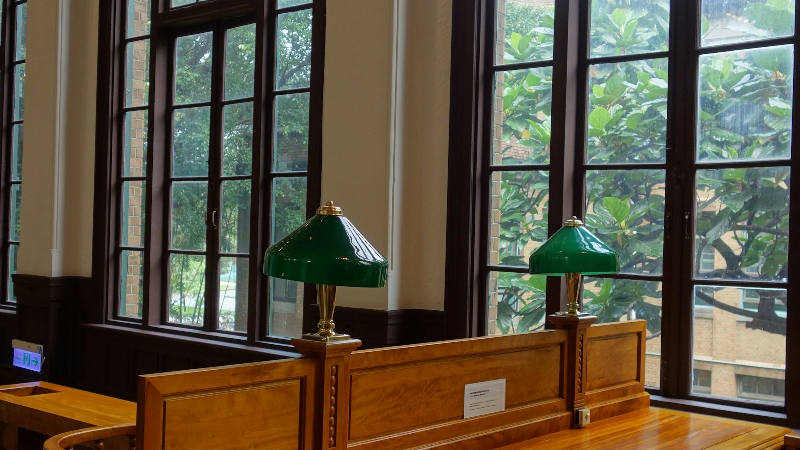 Wide view of a wood-paneled reading room with green library lamps and tall windows