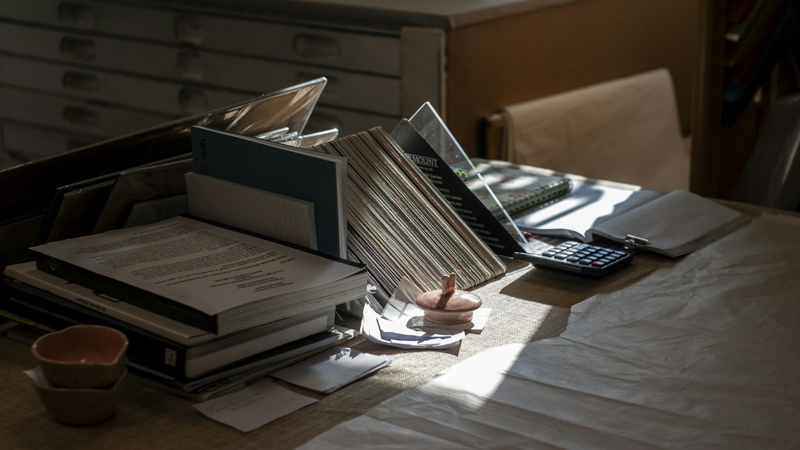 Wide view of a calm desk with stacked books, papers, and a calculator in warm light