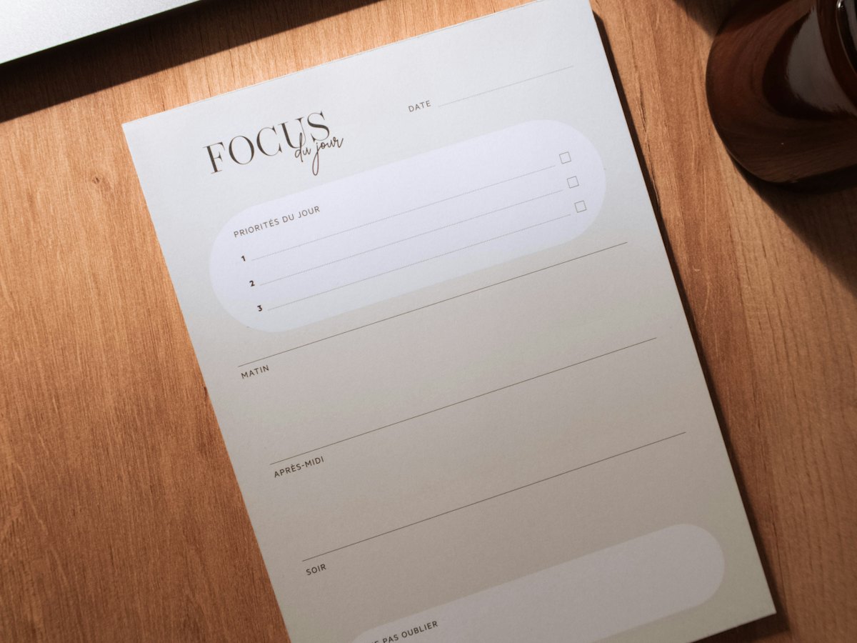 A laptop and a daily planner notepad on a sunlit wooden desk